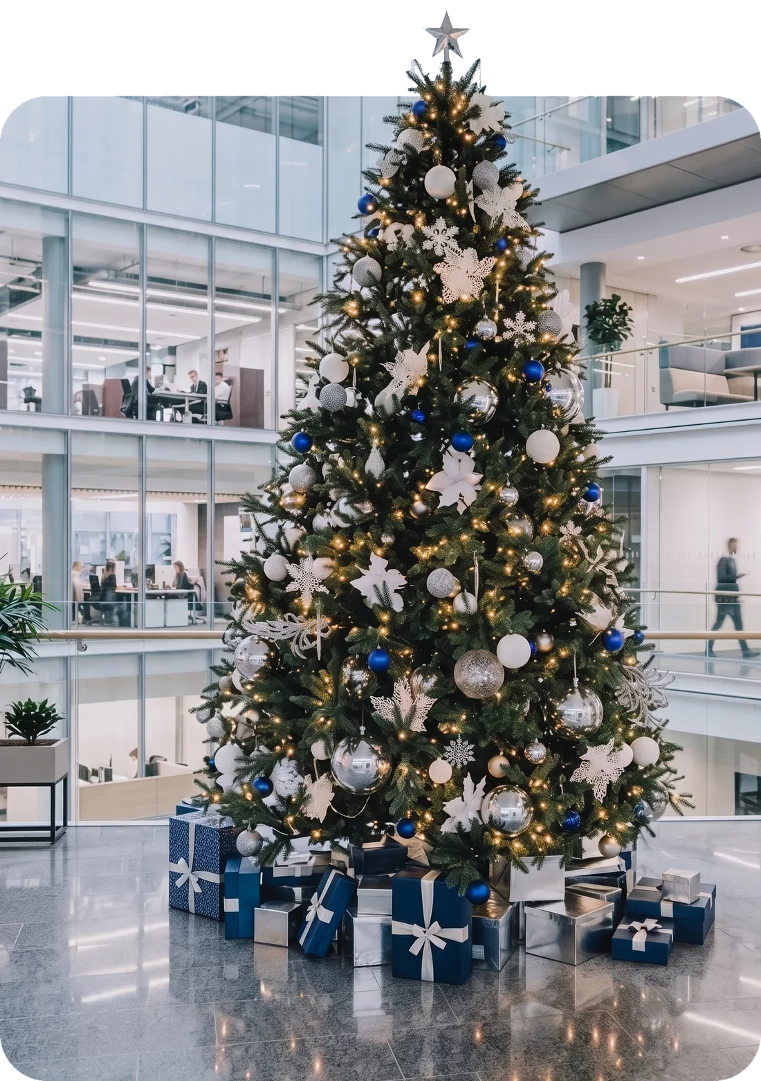 Grand sapin de Noël décoré de boules argent et bleu nuit, installé dans le hall d'une entreprise